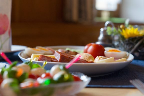 Ein Frühstückstisch mit Aufschnitt, Käse, Tomaten und buntem Obstsalat.