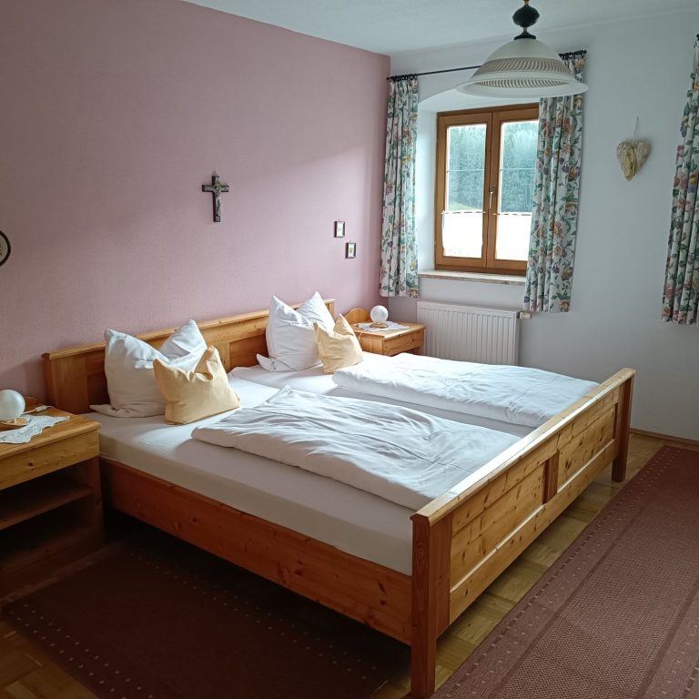 Helles Schlafzimmer mit Doppelbett, Holzmöbeln und Fenstern mit Vorhängen.