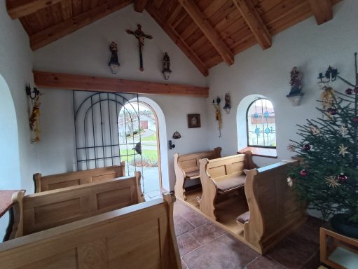 Innenansicht einer kleinen Kapelle mit Bänken, einem Weihnachtsbaum und Fenstern.