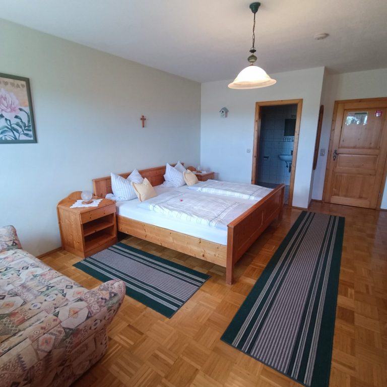 Helles Zimmer mit Doppelbett, Sofa und Holzfußboden, dekoriert mit Teppichen.