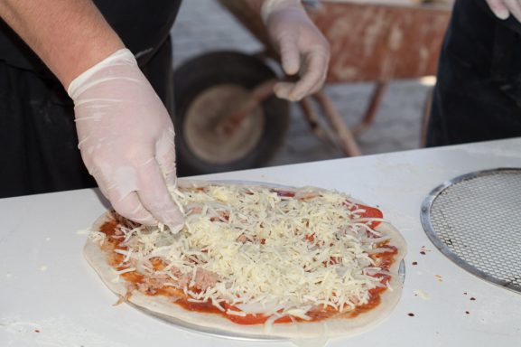 Hände belegen eine Pizza mit Tomatensauce und Käse.