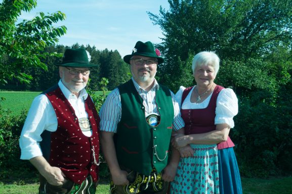 Rupert Vodermaier und Eltern in traditionellen Trachten stehen im Freien vor einer grünen Landschaft.