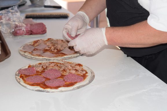 Eine Person belegt zwei Pizzen mit verschiedenen Fleischsorten und Käse.