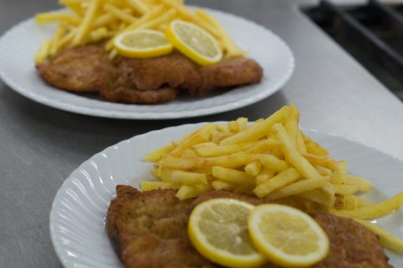 Zwei Teller mit paniertem Fisch, Limettenscheiben und Pommes frites.