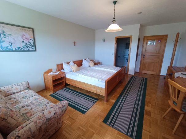 Helles Gästezimmer mit Doppelbett, Sofa und Esstisch, Holzfußboden.