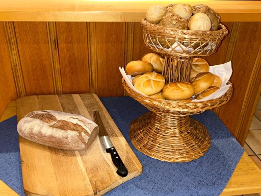 Ein Korb mit Brötchen steht auf einem Holzständer neben einem Laib Brot und einem Messer.