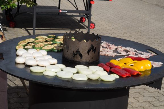 Bunte Gemüsestücke und Fleisch auf einem großen Grill im Freien.