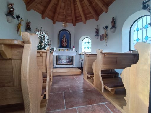 Holzkirchenraum mit Bänken, einem Altar und einer Statue in einem gewölbten Dach.