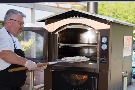 Rupert Vodermaier entnimmt eine Pizza aus einem Holzofen.