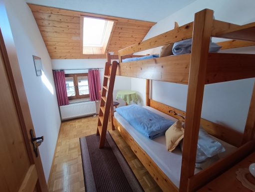 Helles Zimmer mit Etagenbett, Fenster und Holzdetails.