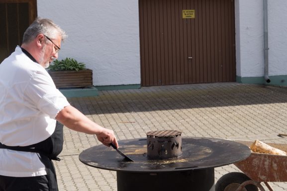 Rupert Vodermaier beim Zubereiten von Speisen an einem großen, runden Tisch im Freien.